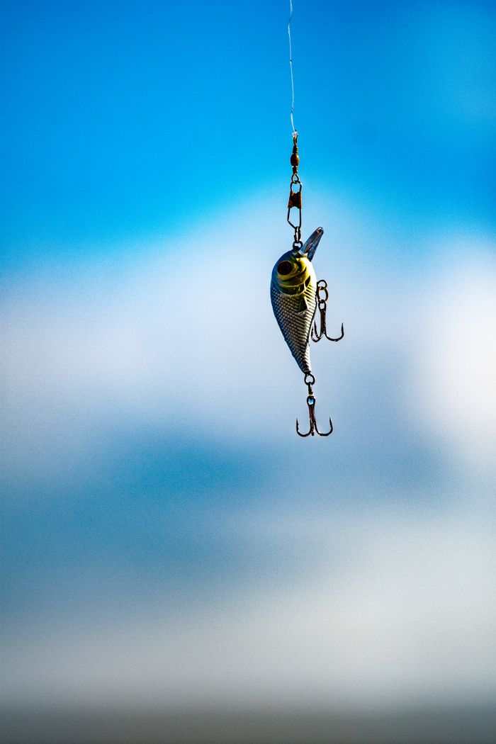 The Art of Drawing Readers In: Your attractive post title goes here Metallic fishing lure with hooks suspended in mid-air against a bright blue sky.